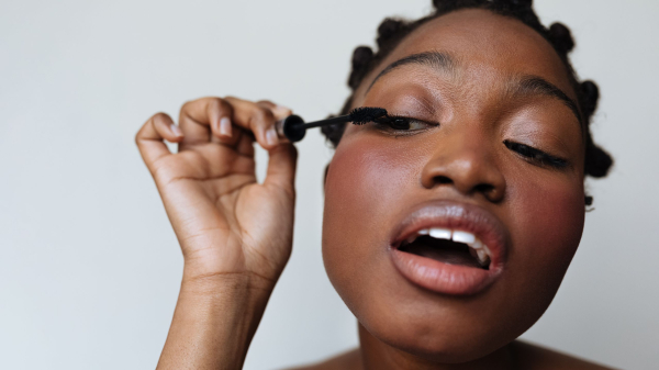 A woman applies mascara to her eyelashes.